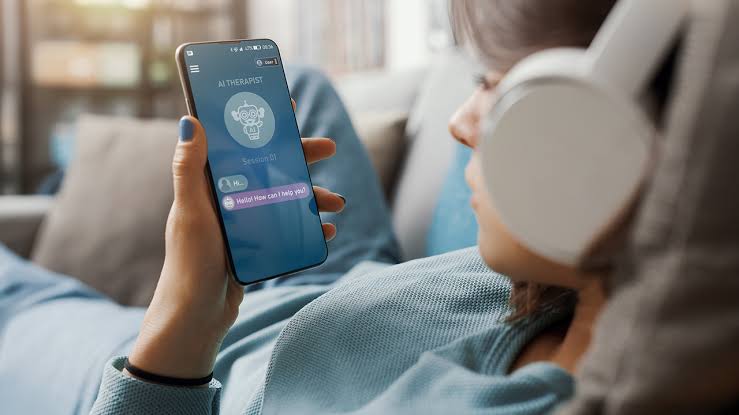 Một người đeo tai nghe trắng sử dụng ứng dụng chatbot nhà trị liệu AI trên điện thoại thông minh khi thư giãn trên ghế sofa tại nhà